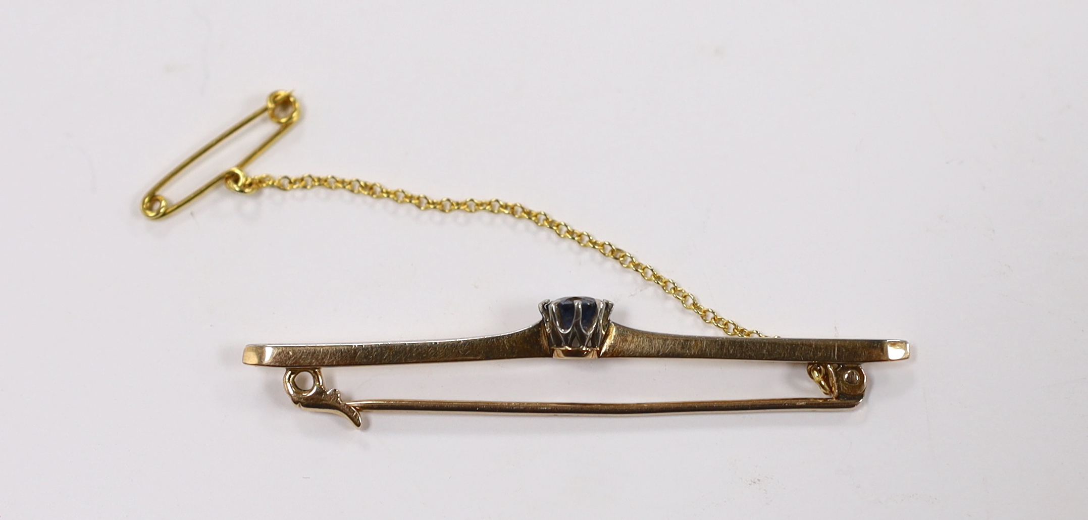An early 20th century yellow metal and single stone sapphire set bar brooch, 57mm, gross weight 4.2 grams, with safety chain.